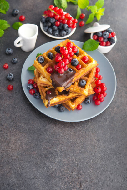Süßes Dessert belgische Waffeln mit Schokolade, Blaubeere und roter Johannisbeere, grüne Minze auf steinigem Hintergrund. Leckeres Frühstück am Morgen. - Foto, Bild