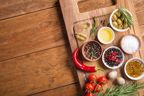 Ingredienti freschi per insalata (sale, pepe, oliva, pomodoro, rosmarino, olio) con tagliere su un tavolo di legno. vista dall'alto - Foto, immagini
