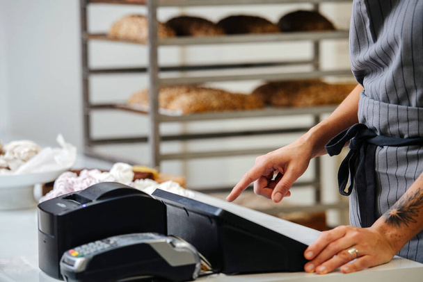Baker standing behing cash register calculating overal cost of the order. Side view. Cropped, no head. - Photo, Image