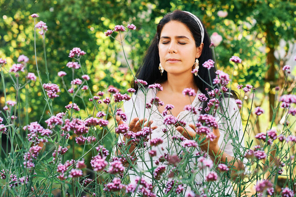 Ritratto all'aperto di donna di mezza età in giardino soleggiato, godendo odore di fiori verbena - Foto, immagini