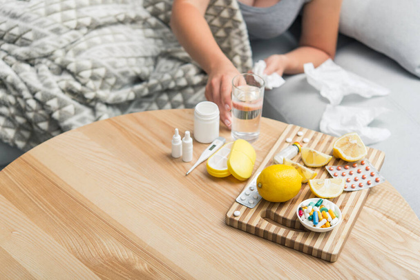 Jovem mulher adoecer frio e gripe foi tratada em casa no sofá. Toma medicamentos e bebidas com um copo de água. - Foto, Imagem