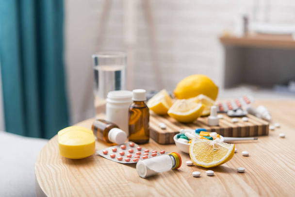 Käsite flunssa hoitoja pillereitä, tabletteja, sitruuna ja lämpömittari kotipöydässä. - Valokuva, kuva