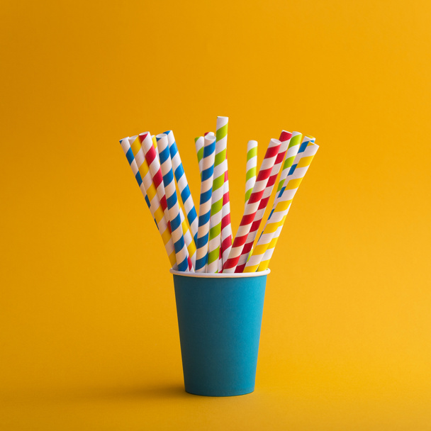 Яскрава кольорова коктейльна солома в паперовій чашці на кольоровому фоні. переробка екологічної концепції. стиль поп-арт
. - Фото, зображення