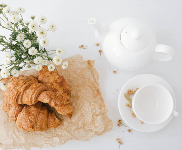 Horní pohled na bílý šálek a konvici s chutnými croissanty na světlém stole. - Fotografie, Obrázek