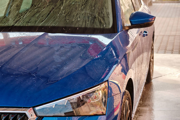 Cerrar la capucha y el faro de un coche azul en unas gotas de agua después de lavar el coche. Limpiar el coche después de lavado de agua de alta presión.  - Foto, Imagen