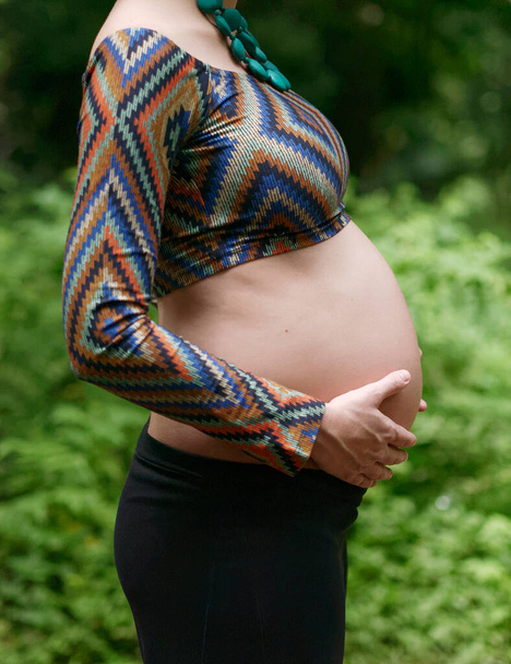 Sluiten van zwangere moderne jonge vrouw aanraken van haar buik buiten. - Foto, afbeelding