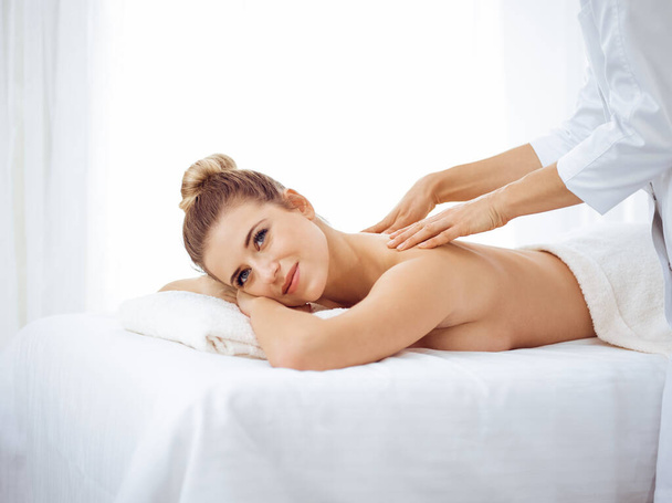 Young and blonde woman enjoying massage of back in spa salon. Beauty concept - Fotó, kép