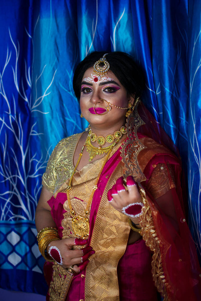 Portrait of a cute Indian model in Bridal look with heavy gold jewelry and red sari - Photo, Image