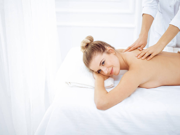 Young and blonde woman enjoying massage of back in spa salon. Beauty concept - Foto, afbeelding