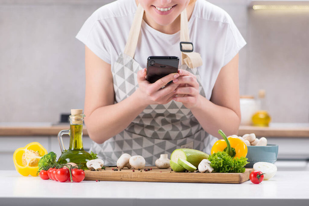 Γυναίκα blogger τροφίμων πυροβολεί περιεχόμενο στην κάμερα στην κουζίνα με φρέσκα λαχανικά σε ένα τραπέζι. Blog για υγιεινή διατροφή. Βήμα-βήμα συνταγές πιάτα. Κινητή φωτογραφία. - Φωτογραφία, εικόνα