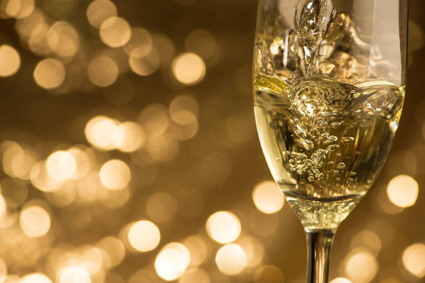 Αφρώδης λευκή σαμπάνια χύνεται σε ένα ποτήρι σε ένα χρυσό φόντο bokeh κύκλους. Χριστούγεννα και Πρωτοχρονιά γιορτή διακοπών. - Φωτογραφία, εικόνα