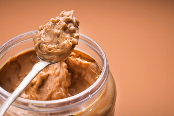 Spoon with peanut butter on a brown background - Foto, afbeelding