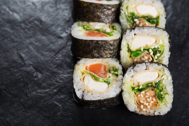 Nahaufnahme einer Sushi-Rolle mit Lachs auf schwarzem Schiefergrund. Japanische Speisekarte - Foto, Bild