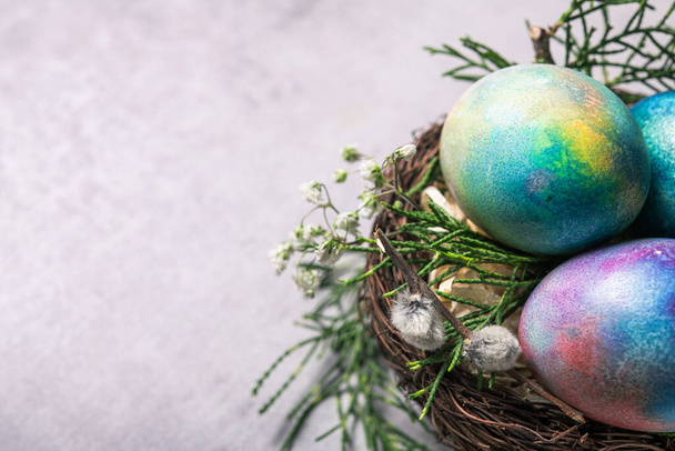 Mystical coloring Easter eggs with twigs and spring flowers in a decorative nest on a gray stone background. - Фото, зображення