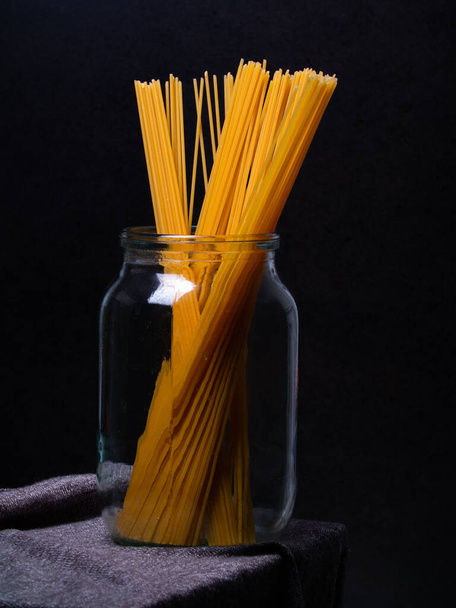 黄色いスパゲティ・マカロニは暗い背景のガラス瓶に入っています。デザイナーにとっては - 写真・画像
