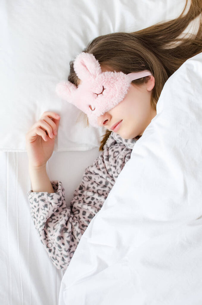 かわいい睡眠マスクと暖かいパジャマを着た美しい若い女性がベッドの上に横になり、午前中に寝ています。トップ表示. - 写真・画像