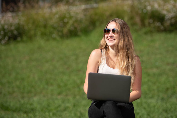 Portrait of a pretty smiling teenager girl working on her laptop with a green background - 写真・画像