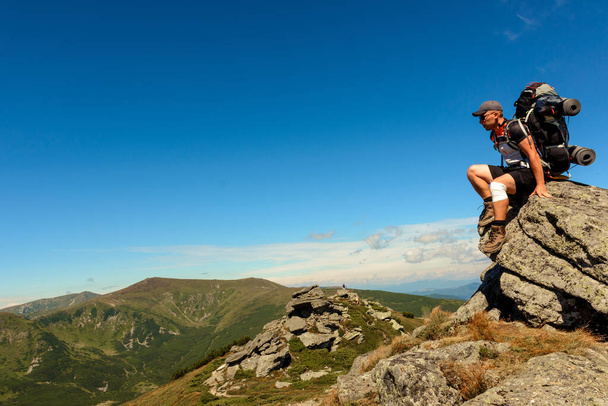 Joven con una mochila de pie en la cima de una montaña y disfrutando de la vista del valle, la cima de los Cárpatos Eared stone.2020 - Foto, Imagen