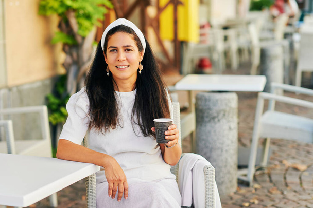 Belle femme hispanique d'âge moyen buvant du café le matin sur la terrasse du café - Photo, image