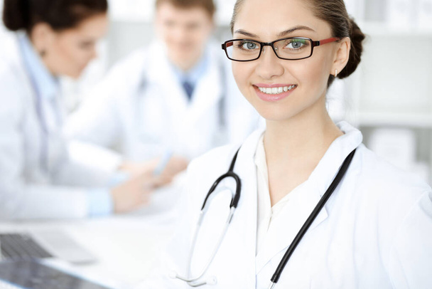 Happy smiling woman-doctor sitting and looking at camera at meeting with medical staff . Medicine concept - Photo, Image