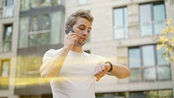 Young blond man talking on the phone looking at the watch, lens flare - Foto, immagini