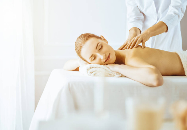 Beautiful woman enjoying back massage with closed eyes in sunny spa center - Foto, Imagem