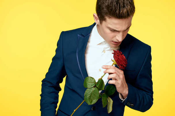 Young man in a classic suit with a red rose in his hand on a yellow background emotions cropped view model - Fotografie, Obrázek