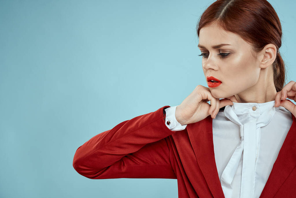 Elegante vrouw in rode jas heldere make-up lippen zelfvertrouwen bijgesneden uitzicht blauwe achtergrond - Foto, afbeelding