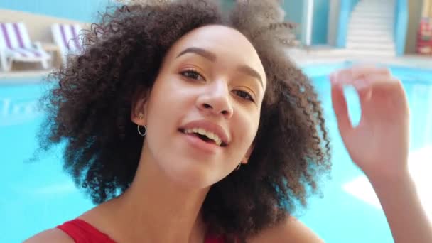Atractiva divertida mujer afroamericana modelo sonríe toothy, endereza el cabello rizado buscando en el dispositivo de la cámara del teléfono, hacer foto selfie, comunicarse en la reunión de conferencia en línea, respuesta en videollamada - Metraje, vídeo