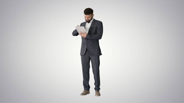 Businessman standing and using tablet computer on gradient backg - Valokuva, kuva