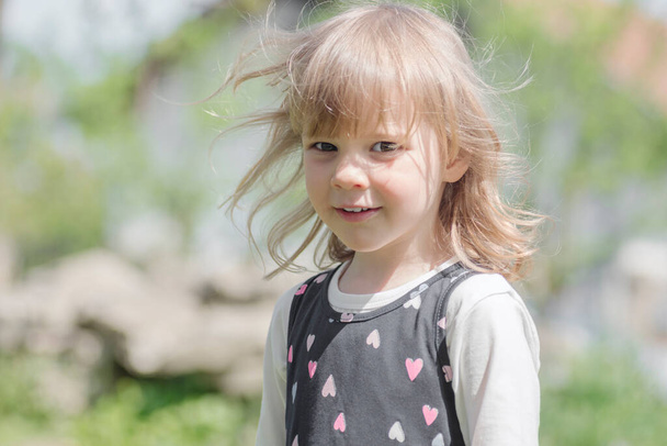 Детский портрет милой белокурой волосы улыбается маленькая девочка на открытом воздухе. - Фото, изображение