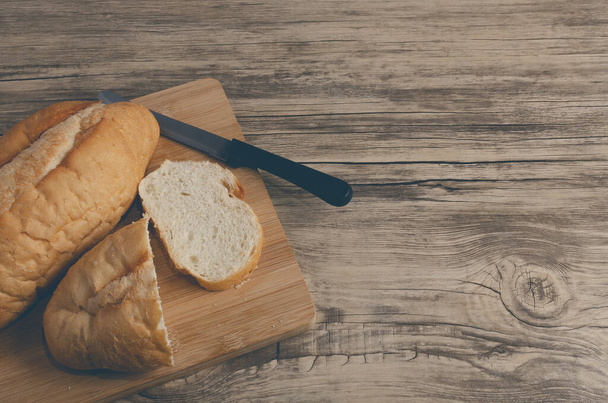Λευκό ψωμί κομμένο σε ξύλο κοπής και ξύλινο τραπέζι. - Φωτογραφία, εικόνα