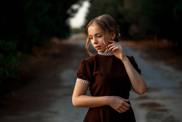 retrato de cerca de una joven hermosa niña en un vestido marrón en un estilo retro en una carretera abandonada. - Foto, Imagen
