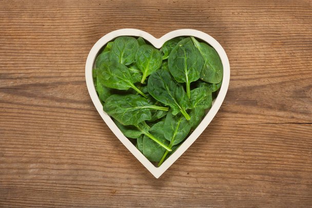 Fresh spinach leaves in a bowl-shaped heart - Zdjęcie, obraz