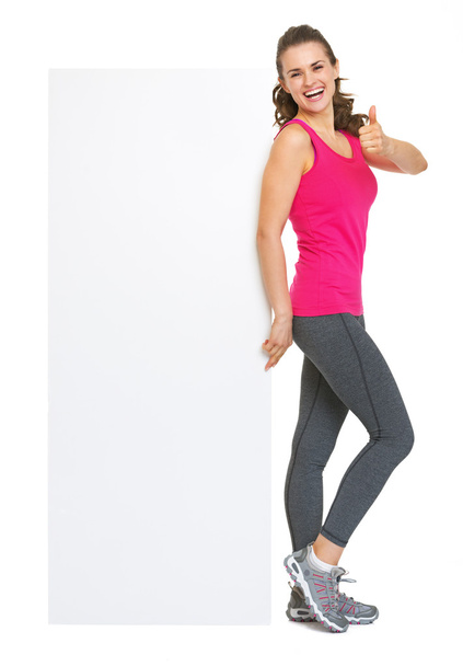 Full length portrait of fitness young woman showing blank billboard and thumbs up - Photo, image