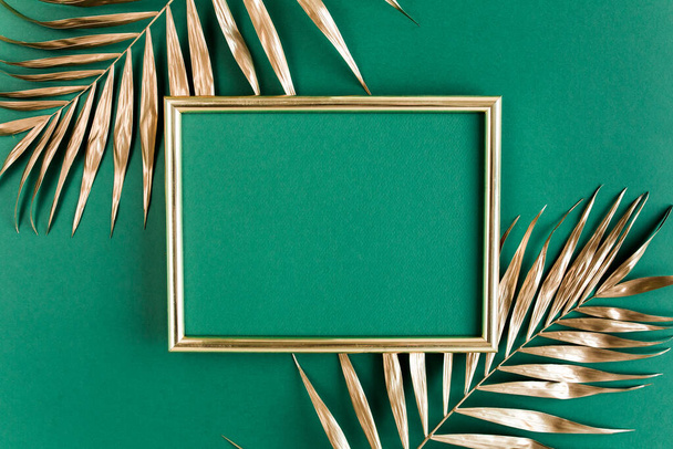 Gold tropical palm leaves and photo frame on green background. Flat lay, top view minimal concept. - Φωτογραφία, εικόνα