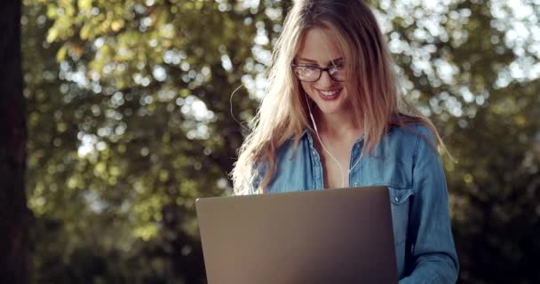 Young woman sitting on grass with laptop and smiling - Video