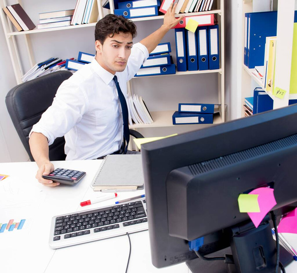 Бизнесмен, работающий в офисе с грудами книг и бумаг - Фото, изображение