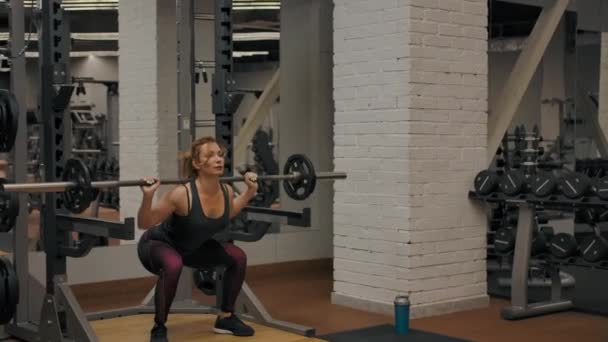 Large panoramique plan horizontal de l'athlète femme faisant des squats d'haltères à l'intérieur de la salle de gym - Séquence, vidéo