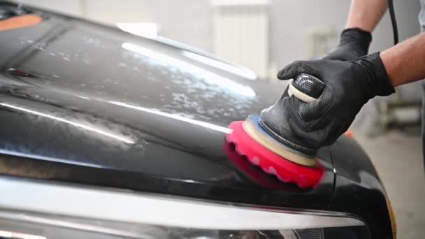 Männlicher Automechaniker poliert eine schwarze Karosserie mit Poliermaschine, um Kratzer zu entfernen - Filmmaterial, Video