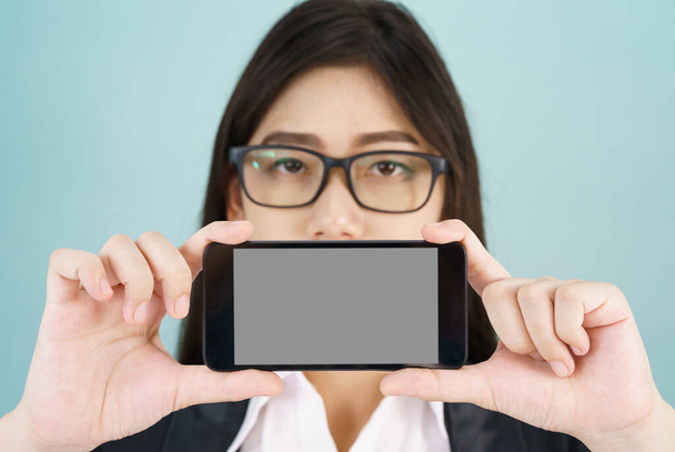 Young women in suit holding her smartphone standing against blue background - Photo, image