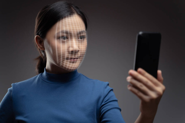 Asijská žena skenuje tvář chytrým telefonem pomocí systému rozpoznávání obličejů. Izolované na pozadí. - Fotografie, Obrázek