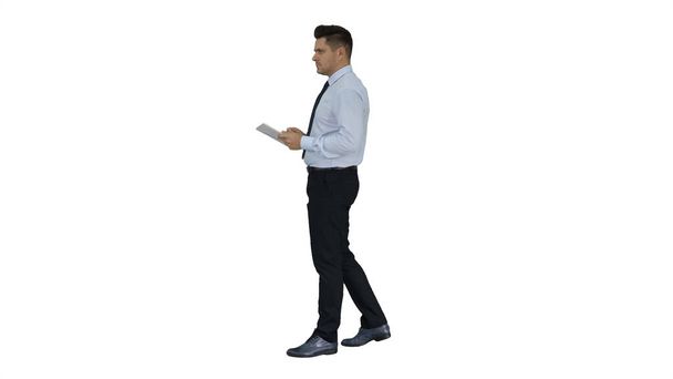 Elegant young businessman using tablet while walking on white background. - Foto, afbeelding