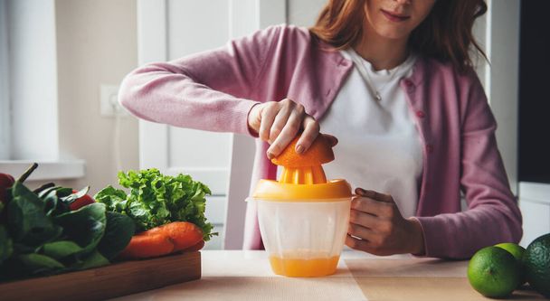 Κοκκινομάλλα γυναίκα συμπίεση χυμό από φρούτα και λαχανικά στο σπίτι, ενώ δίαιτα και αδυνάτισμα - Φωτογραφία, εικόνα