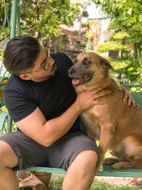 Un hombre mira cómicamente a su perro mascota mientras ambos están sentados en un columpio patio al aire libre. Concepto de mejores amigos. - Foto, Imagen