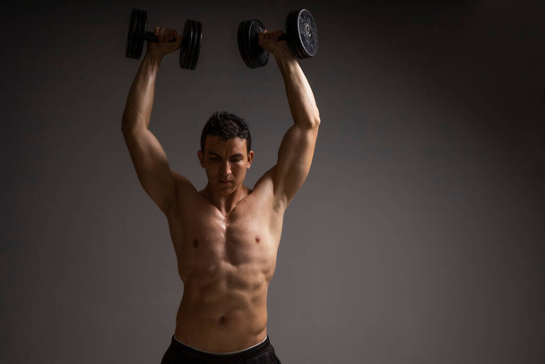 lihaksikas mies tekee olkapään ja käsivarren liikuntaa käsipainoilla - Valokuva, kuva