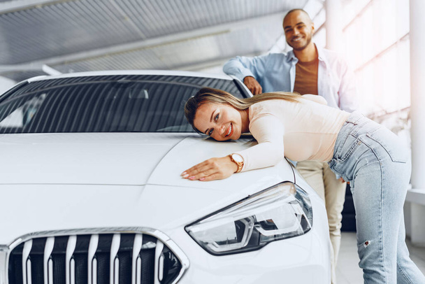 Young couple man and woman hugging their new car in a car shop - Foto, afbeelding