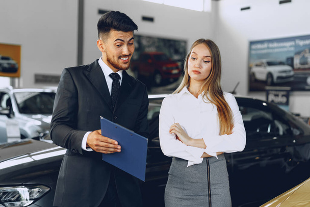 Man car dealer showing a woman buyer a new car - Фото, изображение