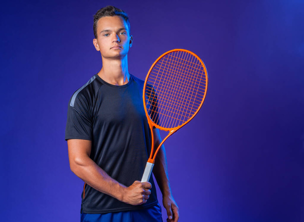 Caucasian young man tennis player posing with tennis racket against purple background - Fotó, kép