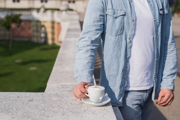 Sokakta kahve fincanı olan genç bir adam, parkta kahve molası. - Fotoğraf, Görsel